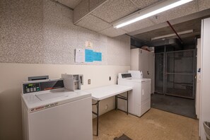 A commercial laundry area with a washing machine, dryer, and a table. - Waikiki Banyan, Top Floor Oceanview Pool + Parking (Honolulu)