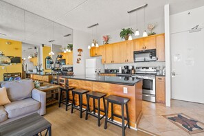 A modern kitchen with a central island, wooden cabinets, stainless steel appliances, and pendant lighting. - Top-Floor Oceanview Waikiki Banyan| Pool Parking (Honolulu)