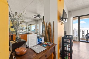 A hotel reception desk with a laptop, brochures, and a wooden bowl. There is a ceiling fan, a large window, and a balcony with a view. - Top-Floor Oceanview Waikiki Banyan| Pool Parking (Honolulu)