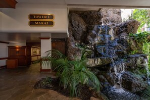 A lobby with a waterfall feature, a sign indicating 'Tower I Makai', and a reception desk. - Top-Floor Oceanview Waikiki Banyan| Pool Parking (Honolulu)