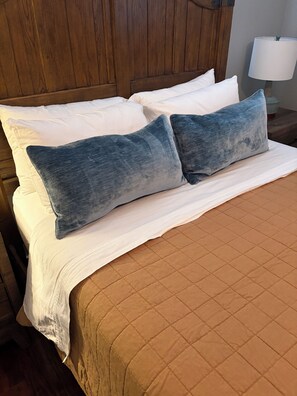A bed with white linens and two blue pillows, a wooden headboard, and a bedside lamp. - Casita Blanca Home Base in San Antonio (San Antonio)