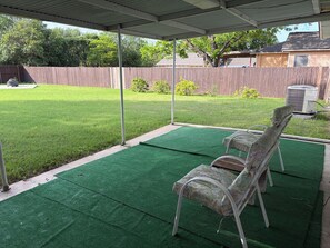 A covered patio area with artificial turf, a metal chair, and a wooden fence in the background. - Casita Blanca Home Base in San Antonio (San Antonio)