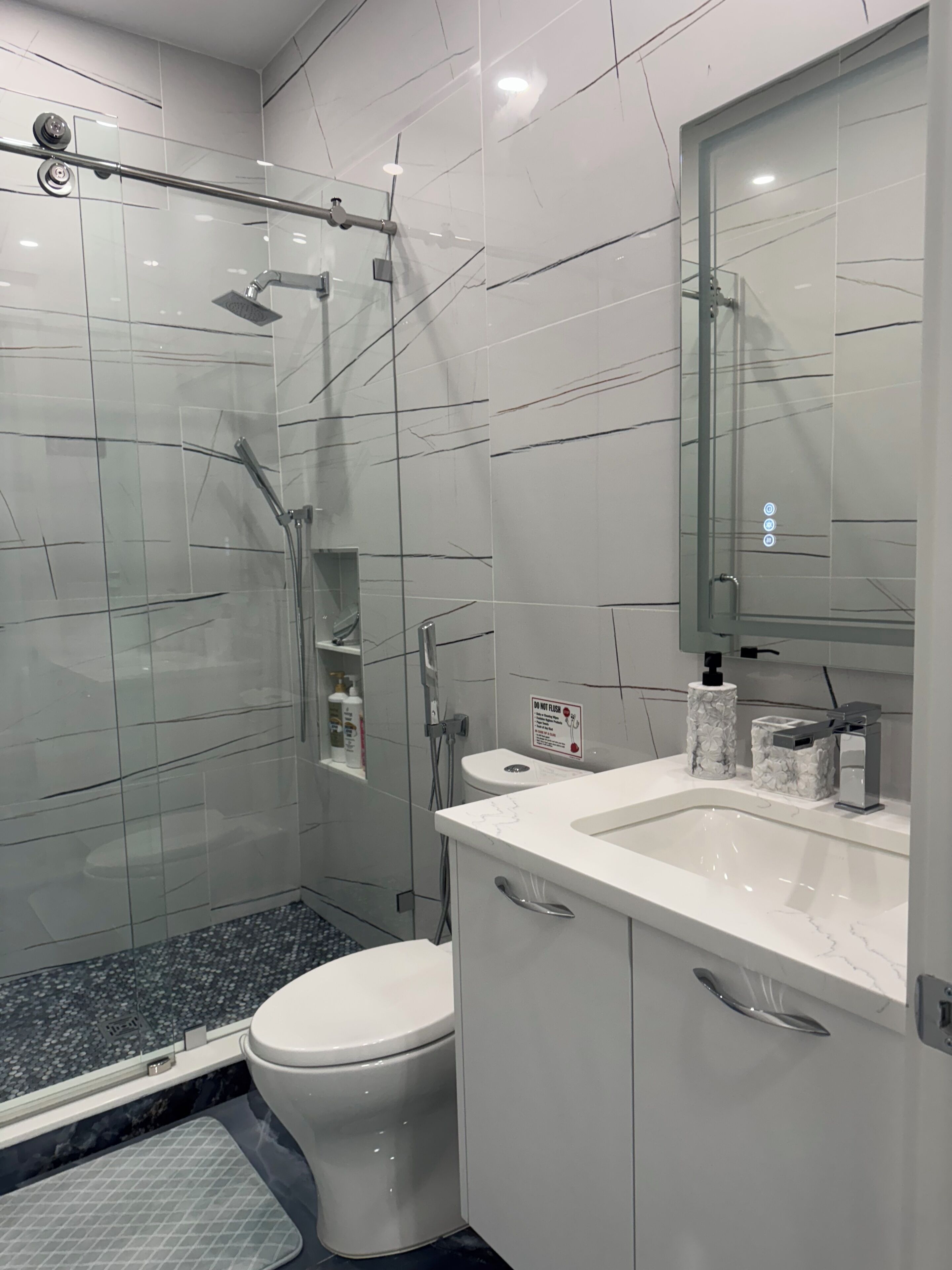 A modern bathroom with a glass-enclosed shower, a toilet, and a vanity with a mirror.