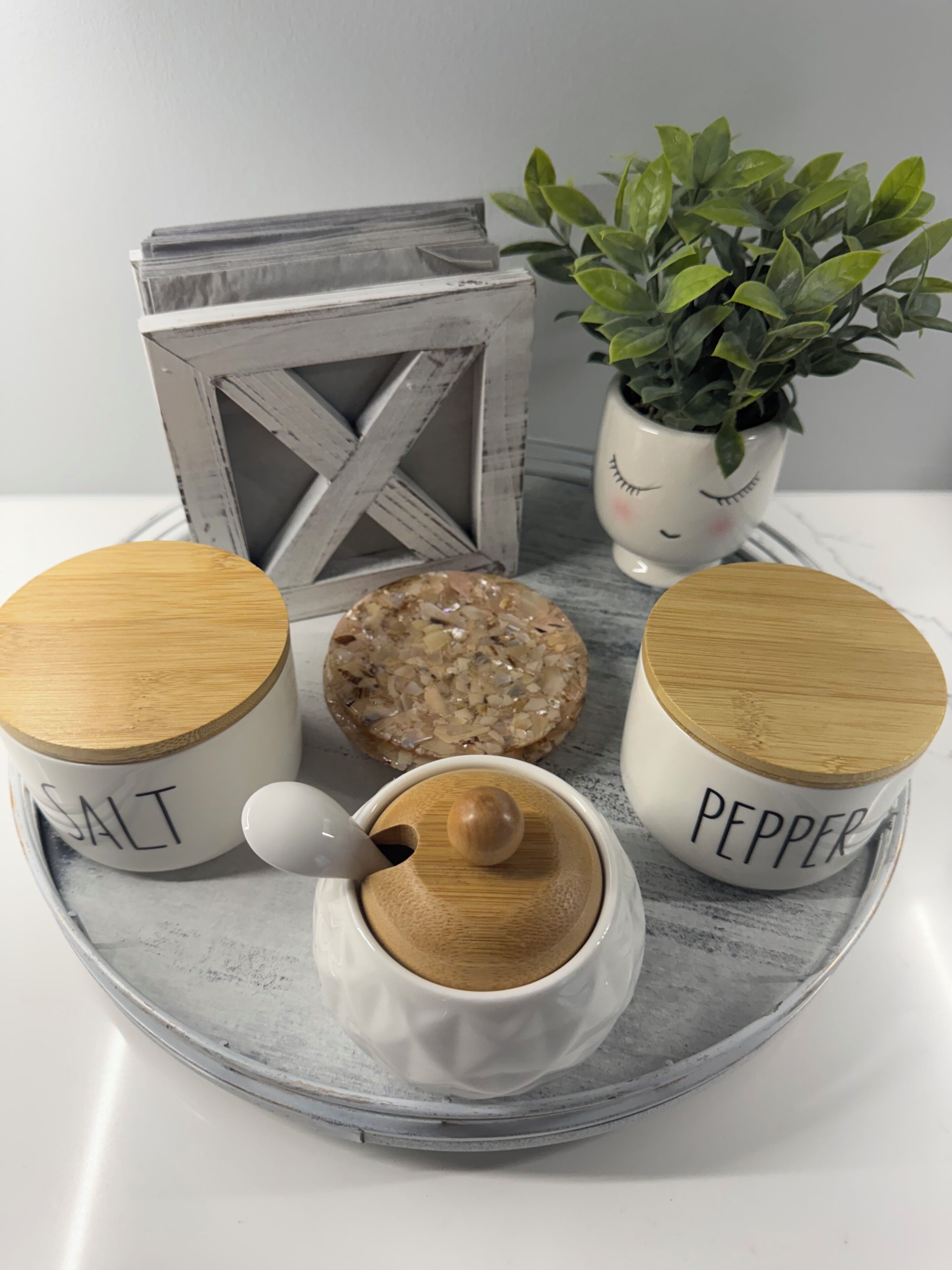 A tray with three containers labeled 'SALT,' 'PEPPER,' and a salt shaker, alongside a decorative plant and a rustic wooden box.