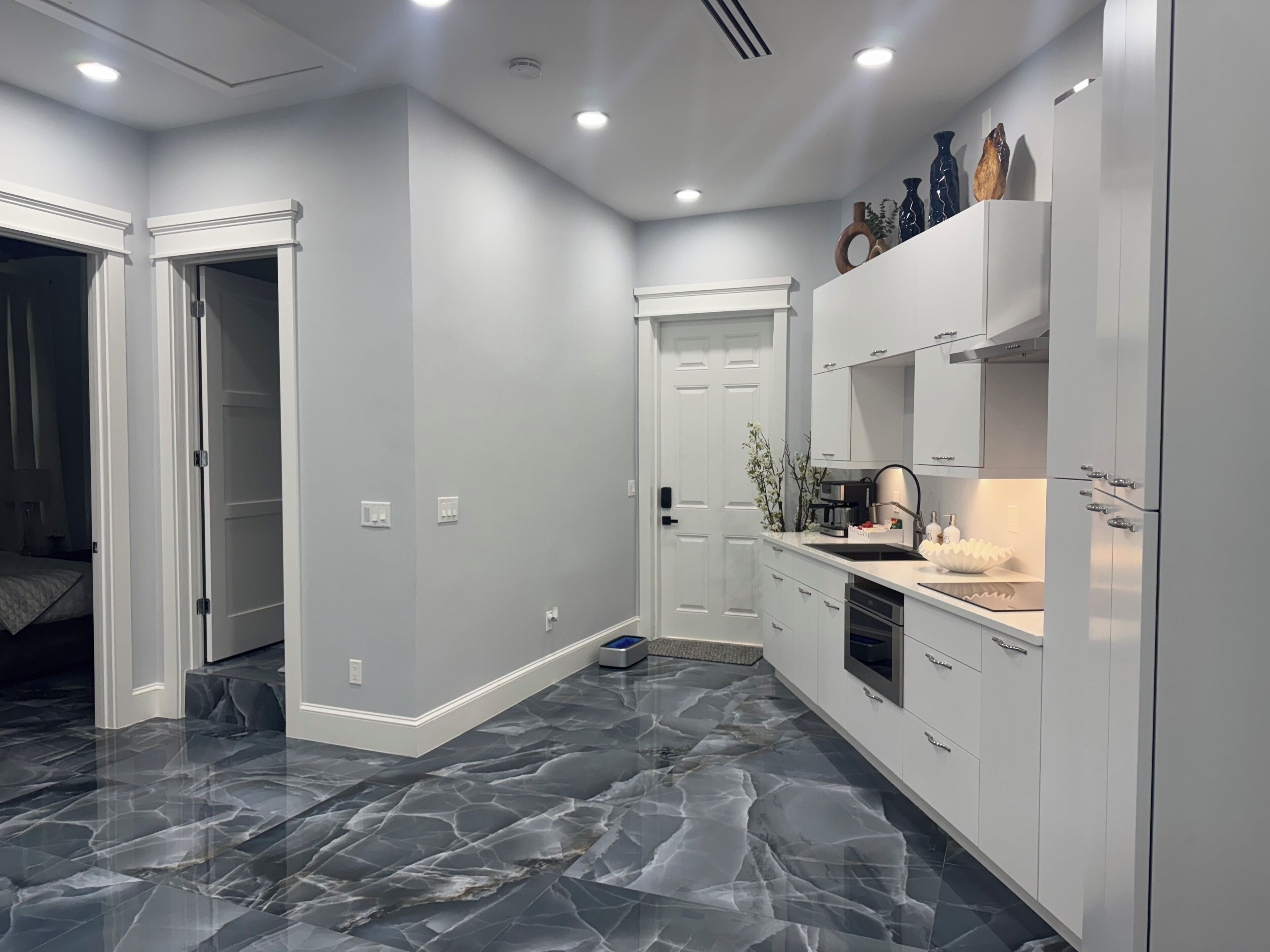 Una cocina moderna con armarios blancos, piso de mármol y horno empotrado.