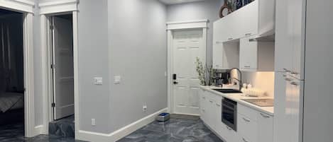 Una cocina moderna con armarios blancos, piso de mármol y horno empotrado.