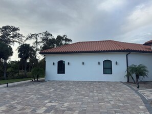 A white building with a tiled roof, arched windows, and a paved driveway.
