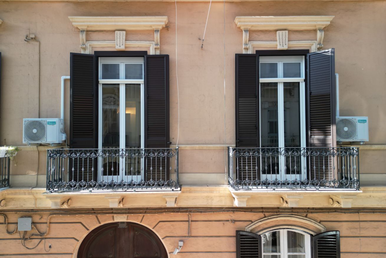A building facade with two windows, each with shutters, and a balcony with a wrought iron railing.