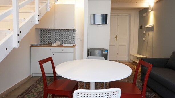 Ein kompakter Wohnraum mit rundem Tisch, zwei Stühlen, einer Couch, einer Treppe, einer Küchenzeile und einem an der Wand befestigten Fernseher.