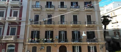 A multi-story building with balconies, a central entrance, and a sign for 'Cluma' on the ground floor.
