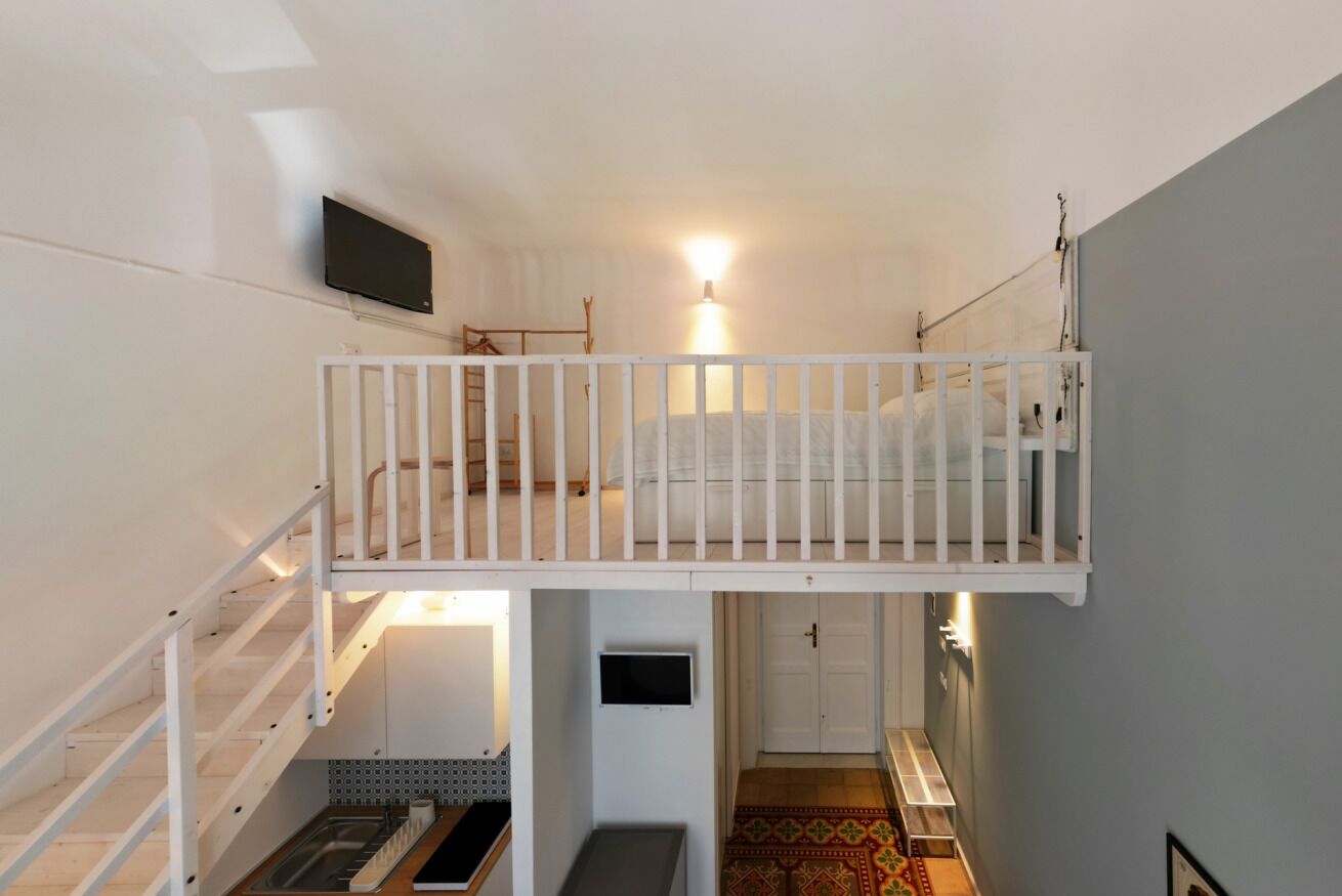 A room with a bunk bed, a television mounted on the wall, a staircase, and a door leading to another room.