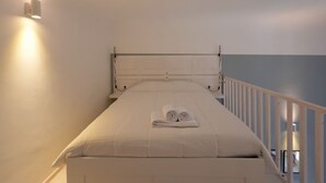Ein Einzelbett mit Kopfteil, eine Wandleuchte und ein weißes Geländer.