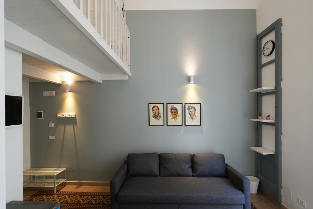 A living room with a grey sofa, a white railing, a wall-mounted clock, and framed artwork.
