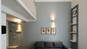 Ein Wohnzimmer mit grauem Sofa, weißer Geländer, einer Wanduhr und gerahmten Kunstwerken.