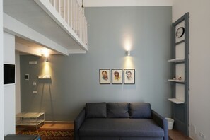 Ein Wohnzimmer mit grauem Sofa, weißer Geländer, einer Wanduhr und gerahmten Kunstwerken.