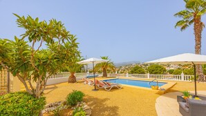 Ein Poolbereich mit Liegestühlen, Sonnenschirmen und Blick auf die Landschaft.