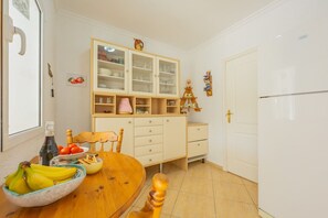 A kitchen with a wooden table, a bowl of fruit, a cabinet with glass doors, and a refrigerator. - Villa Panoramick - Plusholidays (Calpe / Calp)