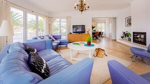 Ein modernes Wohnzimmer mit einer Sofagarnitur, einem Fernseher, einer Kristallleuchtre und einem Kamin.