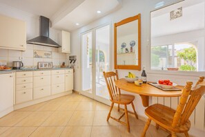 A kitchen with a dining table, chairs, a stove, cabinets, and a window with a view. - Villa Panoramick - Plusholidays (Calpe / Calp)