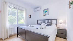 Ein Schlafzimmer mit Bett, Nachttisch, Lampe und einem Fenster mit Vorhängen.