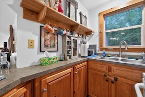 A kitchen with wooden cabinets, a stainless steel sink, and a window with a view of trees. - Near Gettysburg | History, Trails & Dogs (Orrtanna)