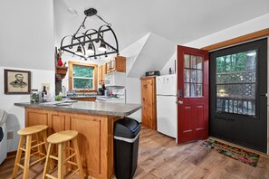 A kitchen with a central island, wooden stools, a black trash bin, and a red door with a window. - Near Gettysburg | History, Trails & Dogs (Orrtanna)