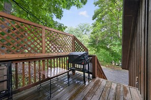 Eine Holzterrasse mit Grill und Tisch, umgeben von einem Gitterzaun und Bäumen.
