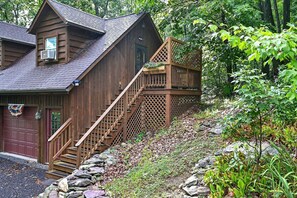 Eine Holz-Blockhütte mit einer Treppe, die zu einer Terrasse führt, umgeben von Bäumen und einer Steinmauer.
