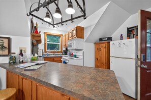 Eine Küche mit einer Granit-Arbeitsplatte, Holzschränken, einem weißen Kühlschrank und einer Pendelleuchte.