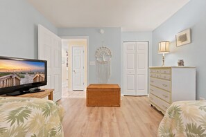 A room with a television, a wicker chest, a dresser, and a dreamcatcher on the wall. - TB 71A First Floor True Blue Condo (Pawleys Island)