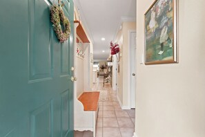 Ein Korridor mit einer türkisblauen Tür, einer Bank, einem roten Blumenschmuck und einem gerahmten Gemälde an der Wand.