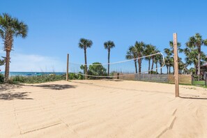 A sandy beach volleyball court with a net, surrounded by palm trees and a clear blue sky. - Ocean front at Ocean reef resort, waterpark, beach (Myrtle Beach)
