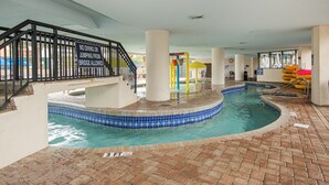En indendørs swimmingpool med et skilt, der forbyder dykning og hop, et legeområde for børn og en gulv belagt med mursten.