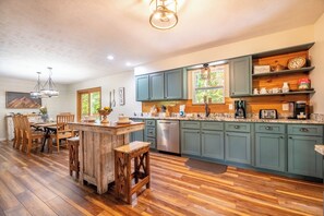 A kitchen with wooden flooring, teal cabinets, and a central island with stools. - Smoky Mtn Home with Theater, Game Room & Hot Tub (Sevierville)