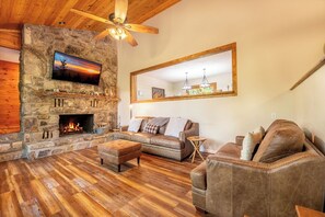 A cozy living room with a stone fireplace, leather sofas, and a large mirror. - Smoky Mtn Home with Theater, Game Room & Hot Tub (Sevierville)