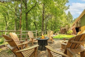 A wooden deck with Adirondack chairs, a central fire pit, and a wooden building in the background. - Smoky Mtn Home with Theater, Game Room & Hot Tub (Sevierville)