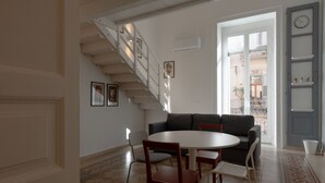 Un soggiorno con una scala, un tavolo rotondo con sedie, un divano e una sveglia appesa al muro.