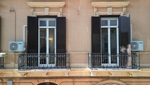 Facciata di un edificio con due finestre, ciascuna con persiane, e un balcone con ringhiera in ferro battuto.