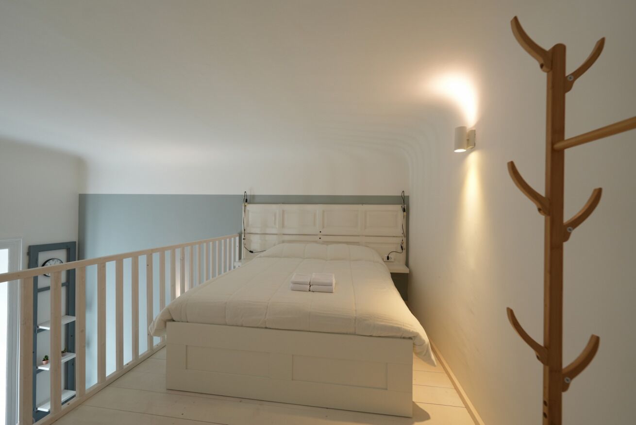 Une chambre à coucher avec un lit, un porte-manteau en bois et une lampe fixée au mur.