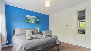 A bedroom with a bed, a painting on the wall, and a door with a view.