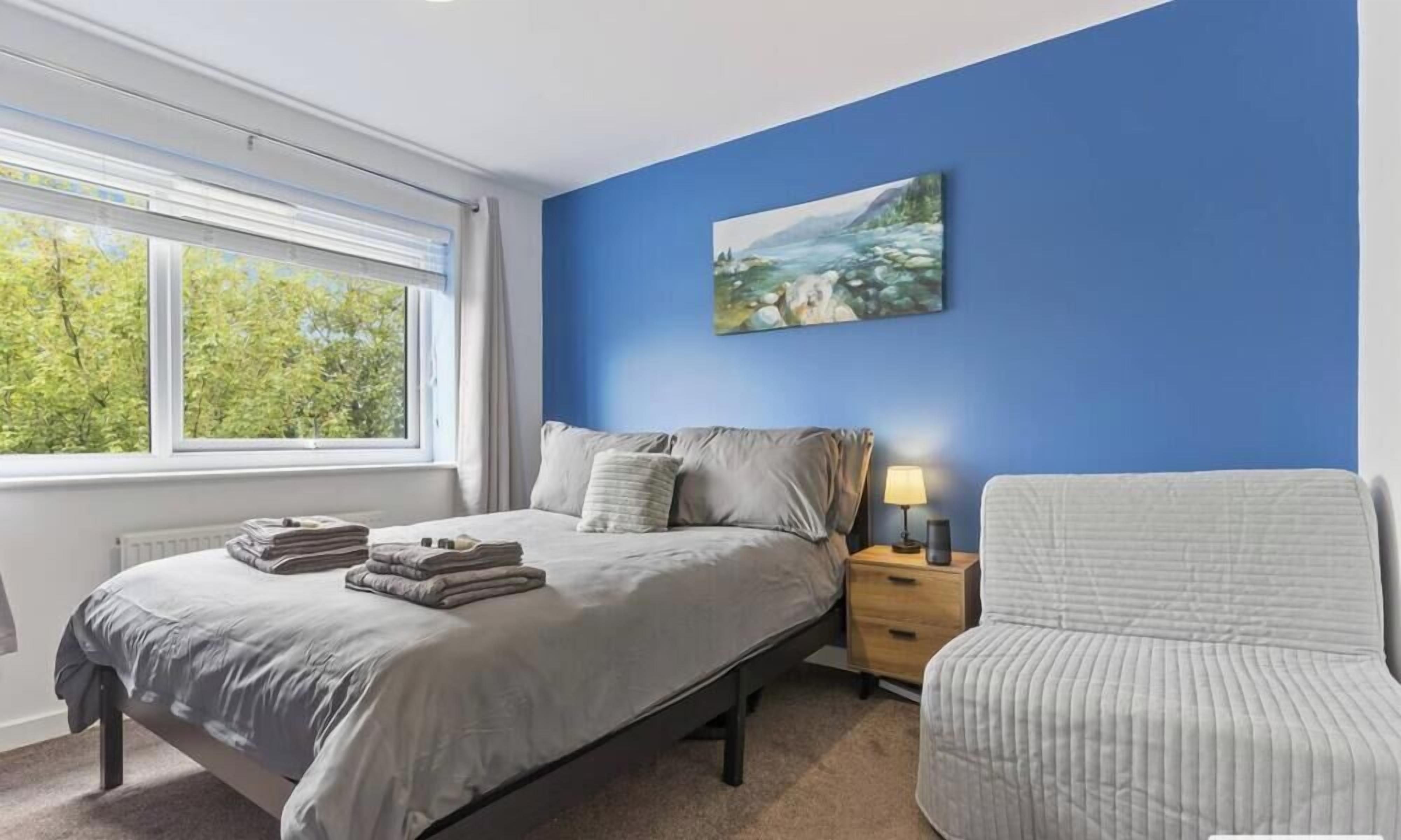 A bedroom with a bed, bedside table, lamp, and a chair.