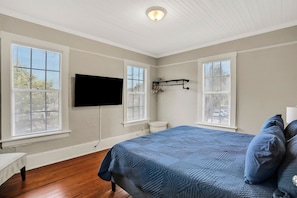 Een slaapkamer met een bed, een aan de muur bevestigde televisie en een raam met jaloezieën.
