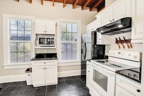 A kitchen with white cabinets, a stainless steel refrigerator, a microwave, a stove, and a window with blinds. - The LaSalle House 3 bedroom in San Marco (Jacksonville)