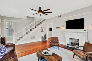 A living room with a fireplace, a TV mounted on the wall, a staircase, and a ceiling fan. - The LaSalle House 3 bedroom in San Marco (Jacksonville)