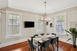 A dining area with a wooden table, chairs, a chandelier, and a flat-screen TV mounted on the wall. - The LaSalle House 3 bedroom in San Marco (Jacksonville)