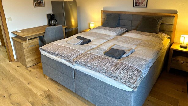 Een slaapkamer met een bed, nachtkastjes, een bureau, een koelkast en een koffiezetapparaat.