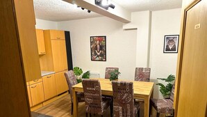 Een eetgedeelte met een houten tafel en stoelen, een keuken op de achtergrond en twee ingelijste foto's aan de muur.