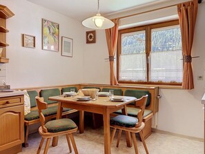 Ein gemütlicher Essbereich mit einem Holztisch und grünen Polsterstühlen, einem Fenster mit Vorhängen sowie einer Wand mit gerahmten Bildern.