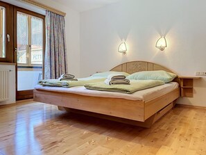 Ein Bett mit Holzkopfteil, zwei Wandleuchten und ein mit Vorhängen drapiertes Fenster.