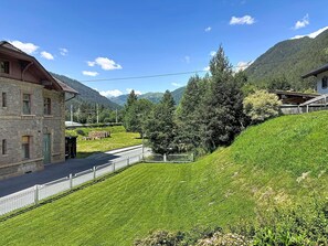 A stone building with a sloped roof, a paved driveway, and a grassy area with trees.